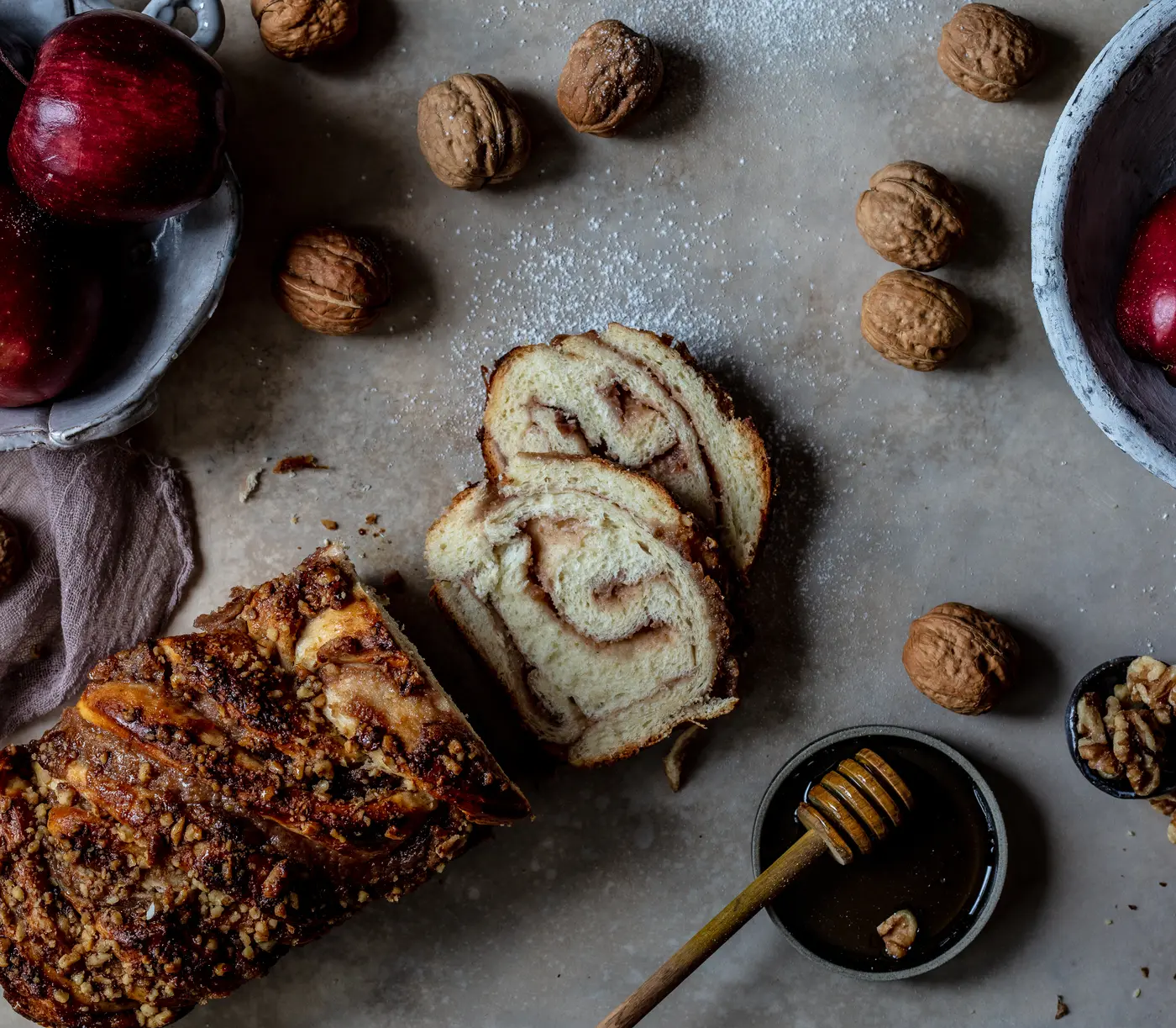 Apple and honey babka with a walnut crumble topping, two slices showing the swirl, red apples and a dish of honey.