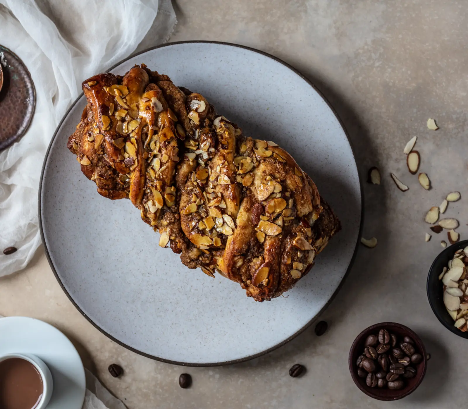Coffee babka with sliced almonds on a grey ceramic plate, a cup of coffee at the edge of the frame.