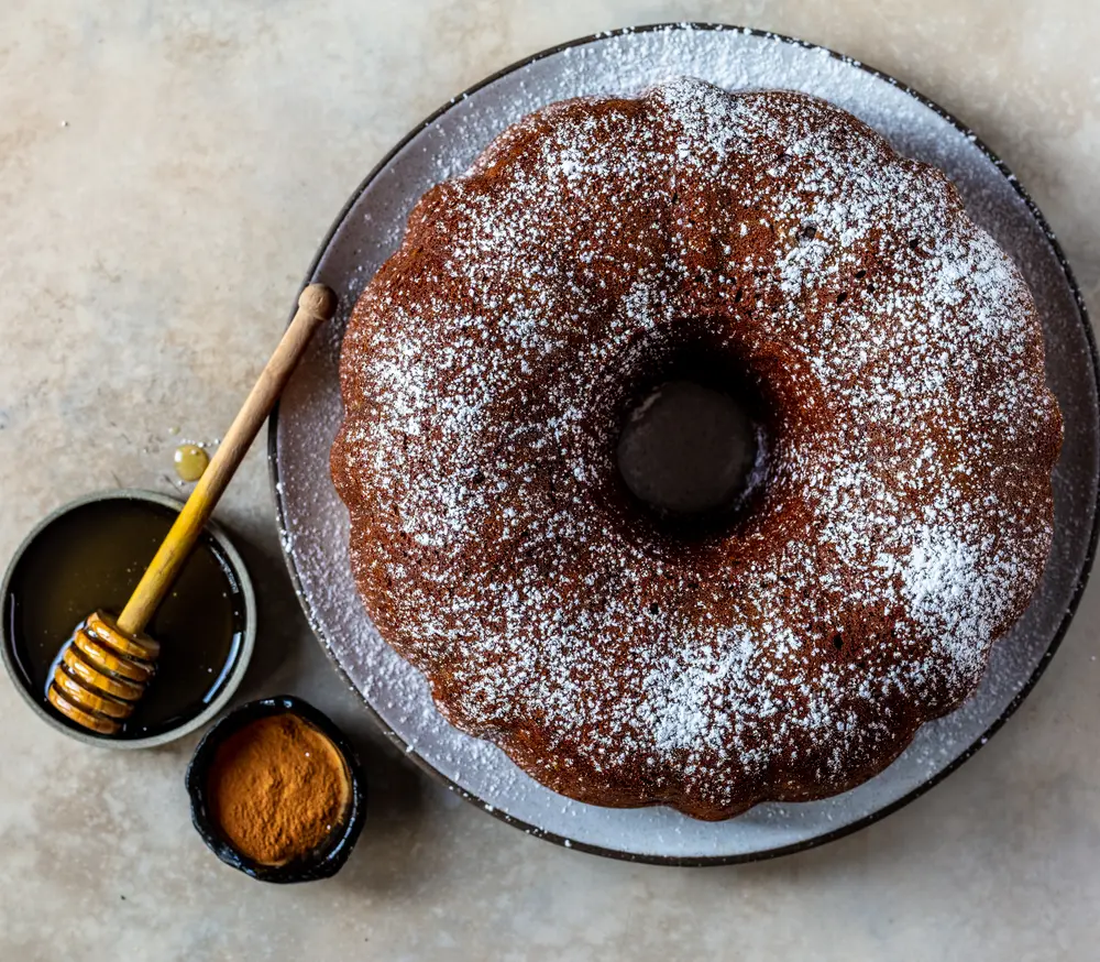 Honey cake dusted with powdered sugar beside a dish of honey.